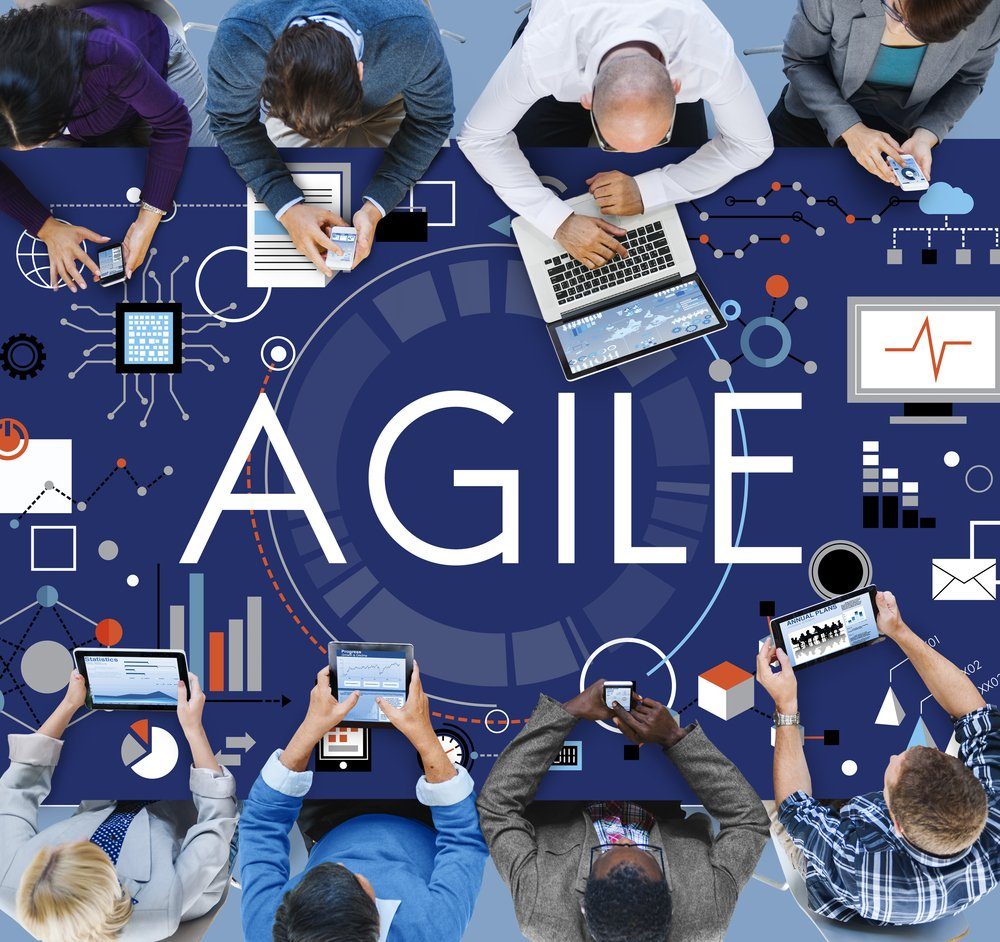 Equipe reunida ao redor de uma mesa com laptops e tablets sob a palavra Agile